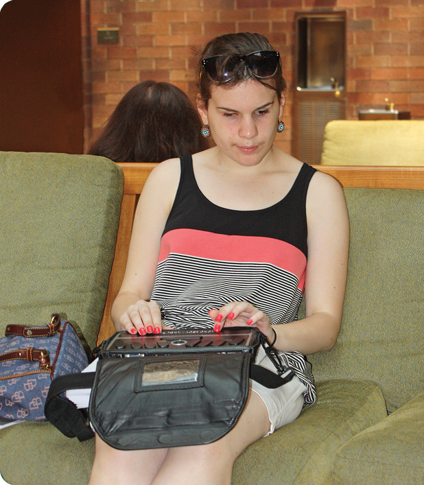 A teen sits on a couch using her Braille writer.